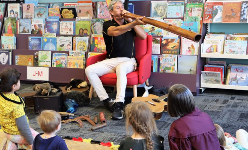 Uncle Amos Simon playing the didgeridoo for an audience of kids at the library